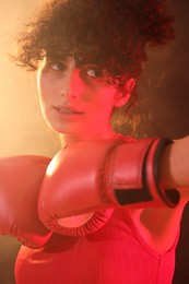 Photo of Beautiful young woman with boxing gloves on color background in neon lights and smoke, closeup