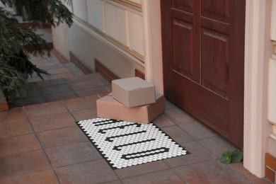 Photo of Cardboard boxes on stylish door mat near entrance