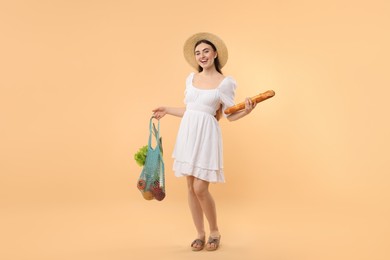 Photo of Woman with string bag of fresh vegetables and baguette on beige background