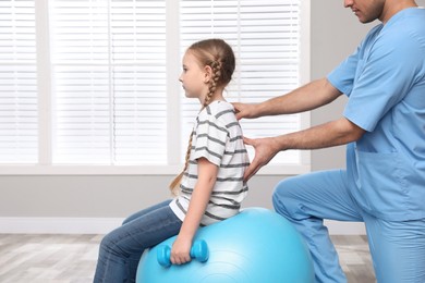 Photo of Orthopedist helping child to do exercise with dumbbell in clinic, closeup. Scoliosis treatment