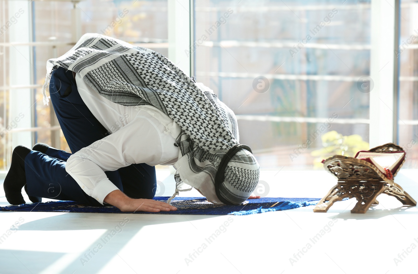 Photo of Muslim man with Koran praying on rug indoors