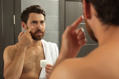 Photo of Handsome man applying cream on face in bathroom near mirror