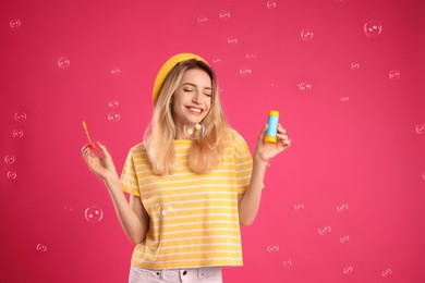 Young woman blowing soap bubbles on pink background