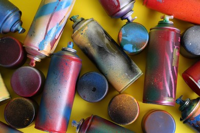 Many spray paint cans with caps on yellow background, flat lay