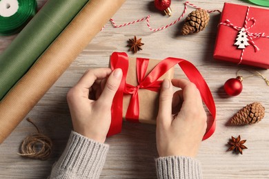 Photo of Woman decorating gift box at white wooden table, top view. Christmas present