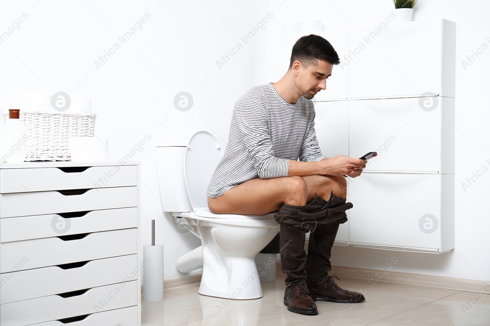 Photo of Man with smartphone sitting on toilet bowl in bathroom