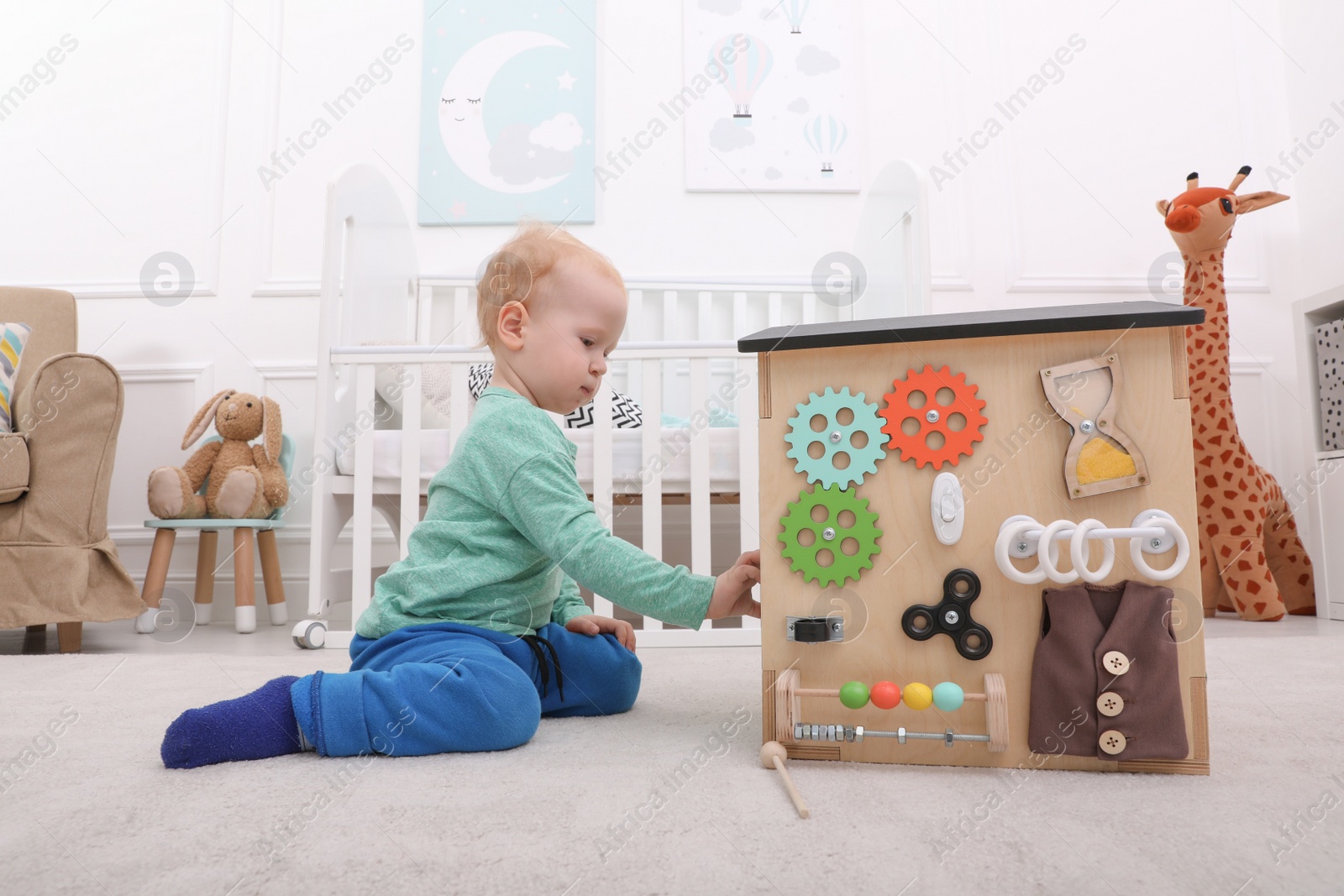 Photo of Cute little boy playing with busy board house on floor at home