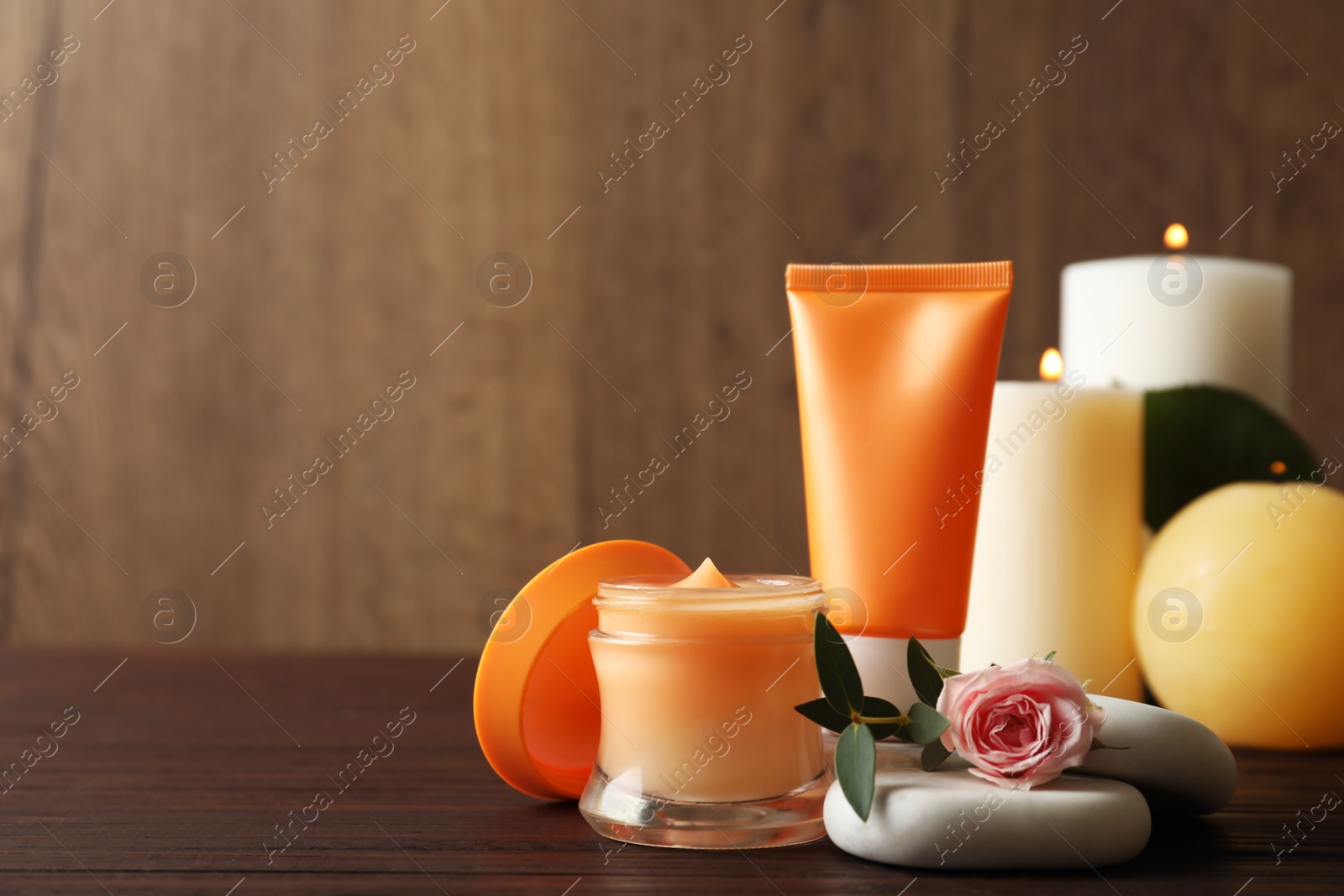 Photo of Composition with cosmetic products, spa stones and burning candles on wooden table. Space for text