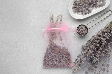 Photo of Scented sachet and dried lavender flowers on light gray textured table, flat lay. Space for text