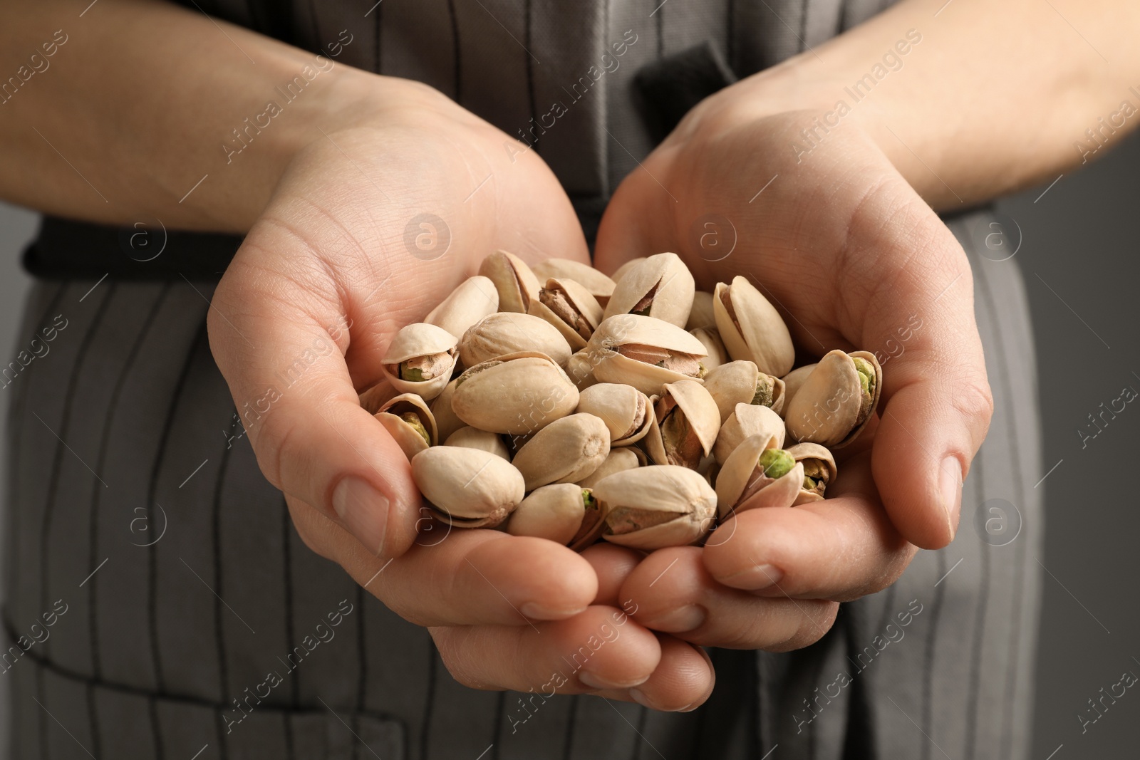 Photo of Woman holding organic pistachio nuts on grey background, closeup