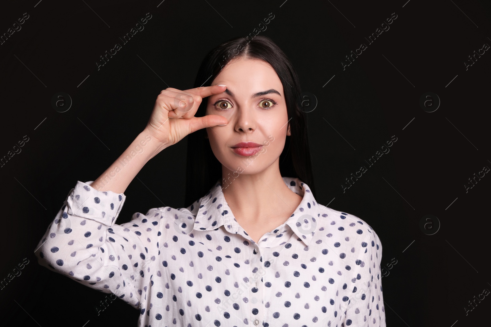 Photo of Woman checking her health condition on black background. Yellow eyes as symptom of problems with liver