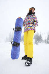 Young woman with snowboard wearing winter sport clothes outdoors, low angle view