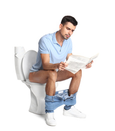 Man with newspaper sitting on toilet bowl, white background