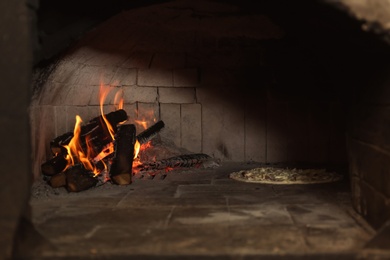 Burning firewood and tasty pizza in oven at restaurant kitchen