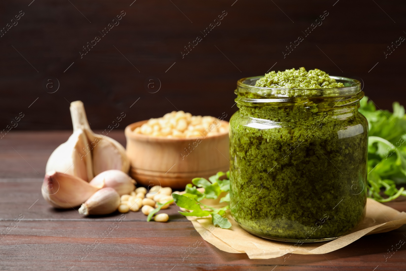 Photo of Jar of tasty arugula pesto and ingredients on wooden table. Space for text