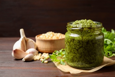 Jar of tasty arugula pesto and ingredients on wooden table. Space for text