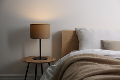 Photo of Stylish lamp on table near bed indoors