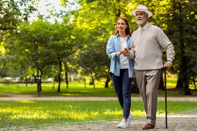 Photo of Senior man with walking cane and young woman in park. Space for text