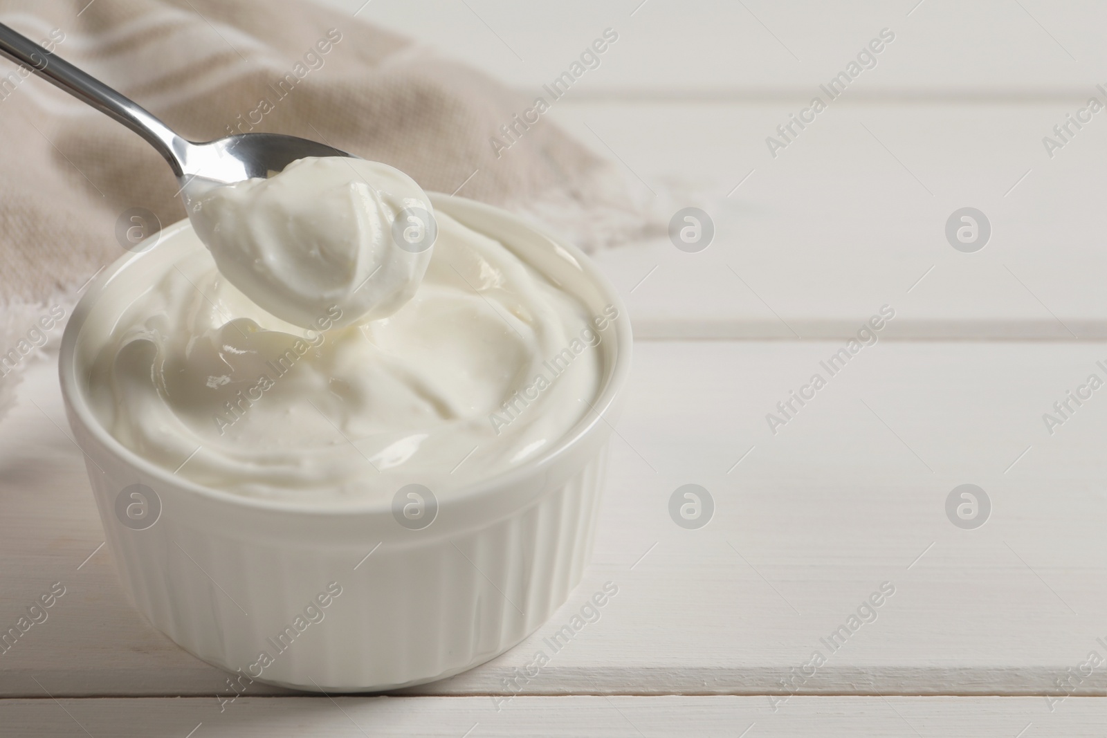 Photo of Taking yogurt with spoon from bowl at white wooden table, space for text