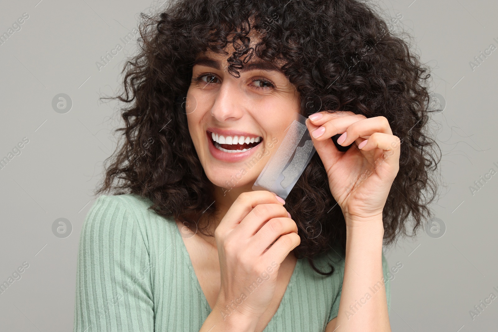 Photo of Young woman holding teeth whitening strips on grey background