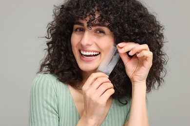 Young woman holding teeth whitening strips on grey background