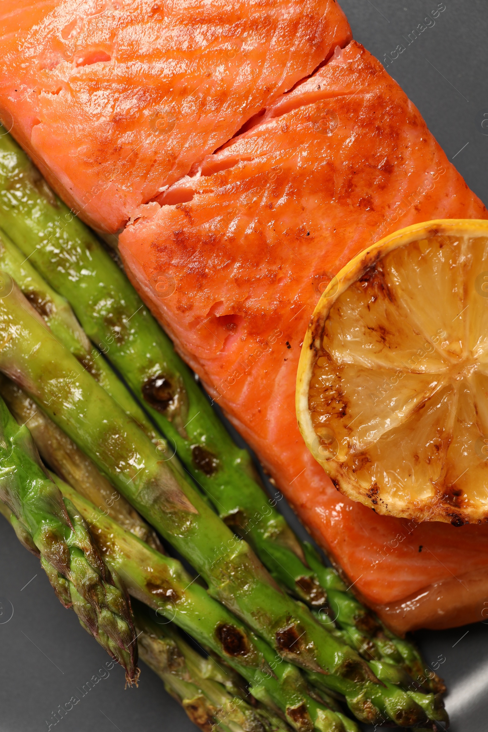 Photo of Tasty grilled salmon with asparagus and lemon on grey plate, top view