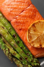 Photo of Tasty grilled salmon with asparagus and lemon on grey plate, top view