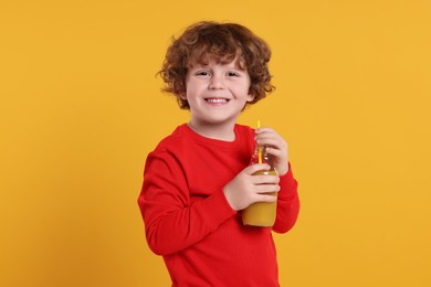 Photo of Cute little boy with glass bottle of fresh juice on orange background