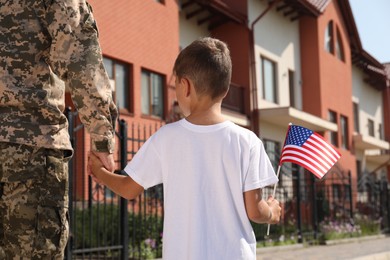Soldier and his little son with American flag outdoors, back view. Veterans Day in USA