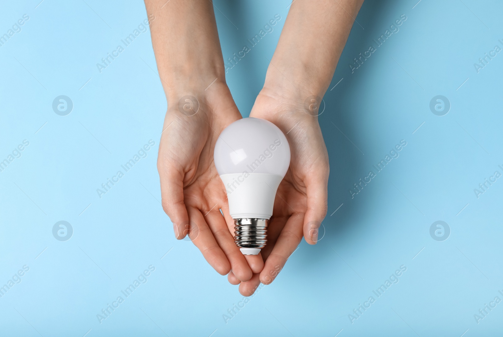 Photo of Woman holding light bulb on color background, top view