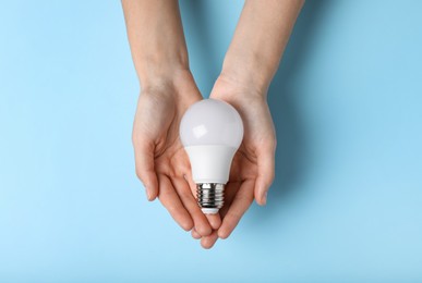 Woman holding light bulb on color background, top view
