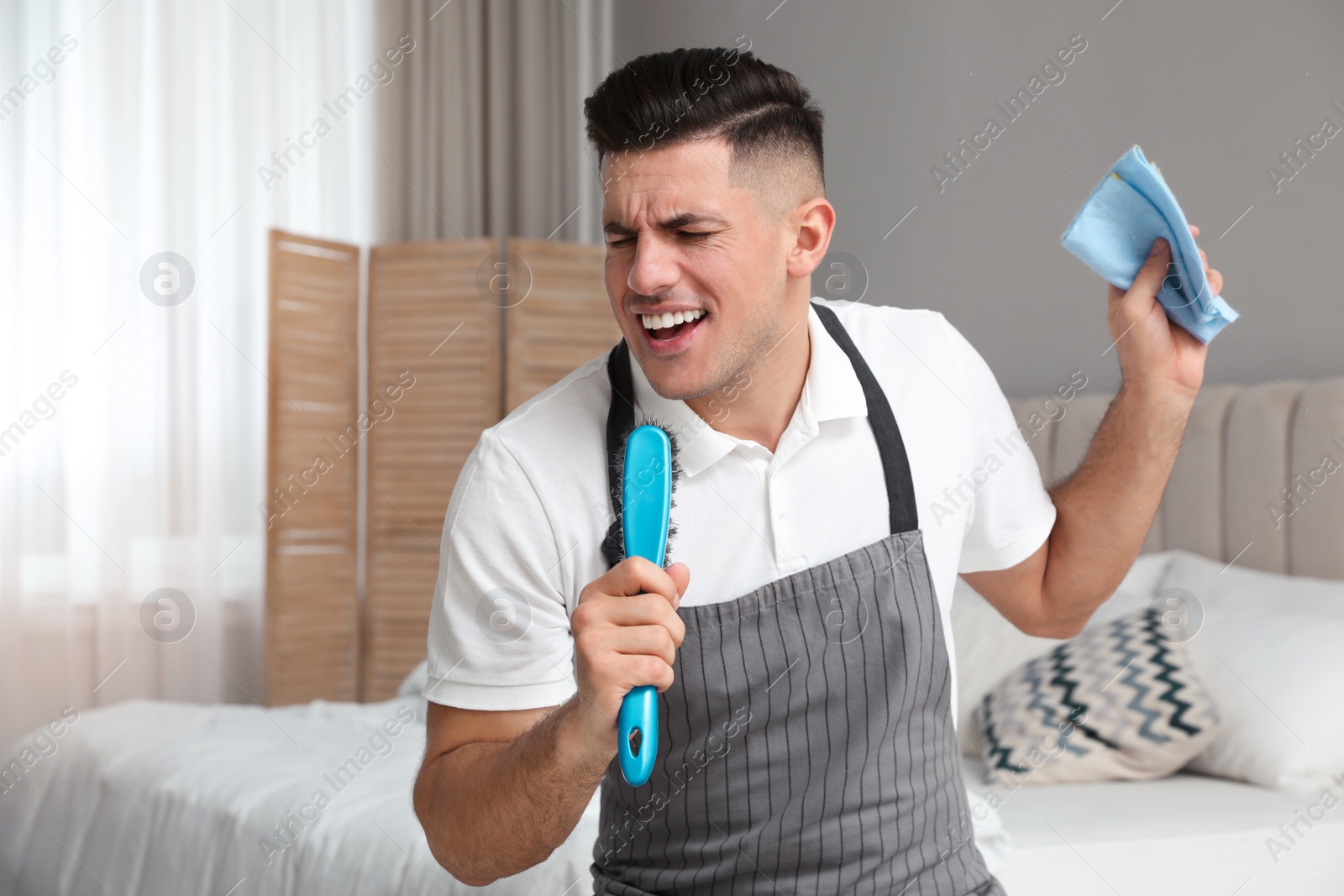 Photo of Man with brush and rag singing while cleaning in bedroom
