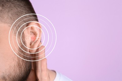 Young man with hearing problem on lilac background, closeup. Space for text