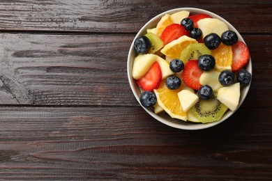 Tasty fruit salad in bowl on wooden table, top view. Space for text