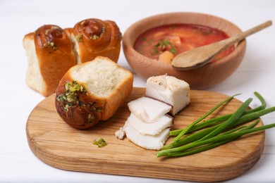 Photo of Delicious pampushky (buns with garlic), green onions and salo served for borsch on white wooden table. Traditional Ukrainian cuisine