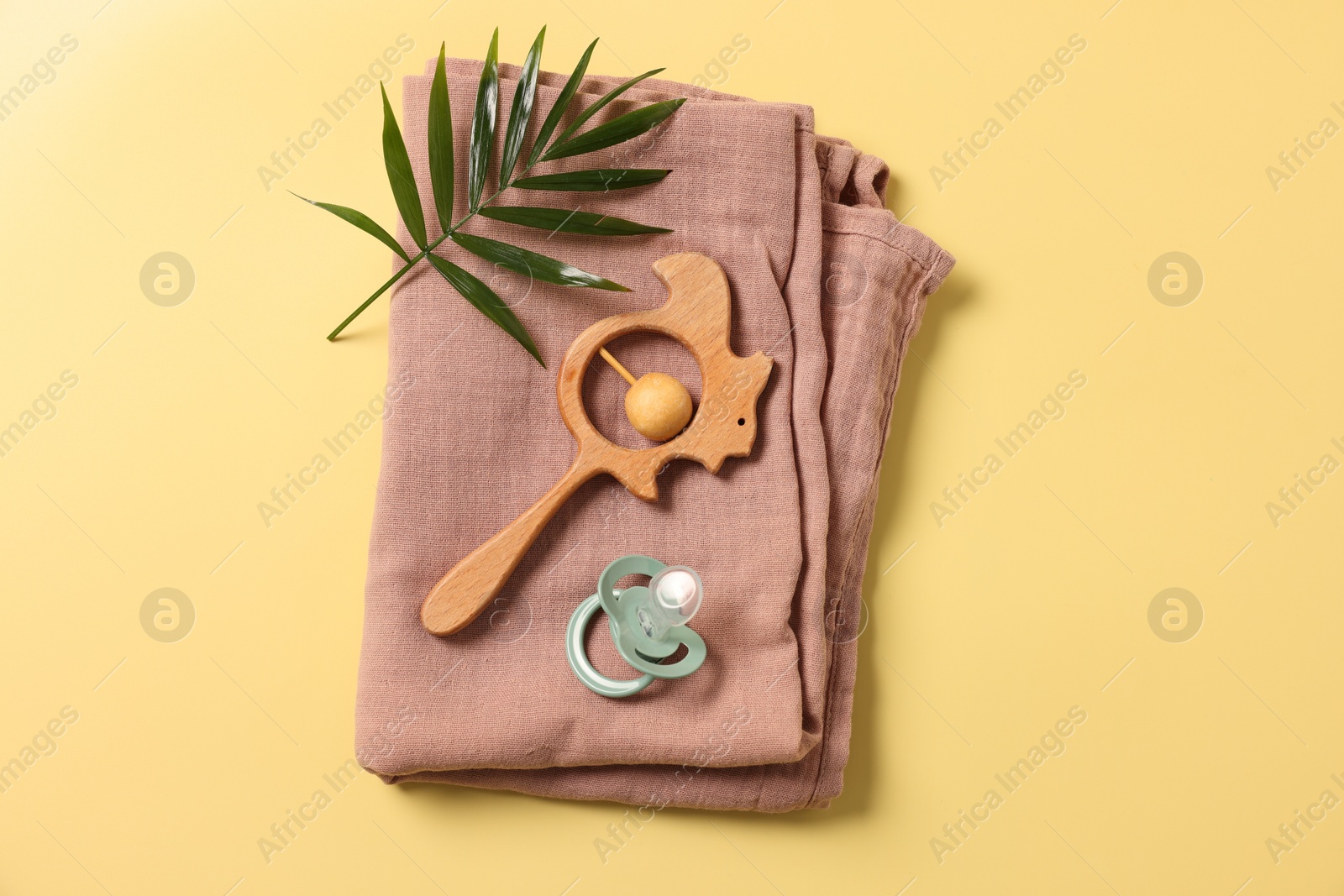 Photo of Baby accessories. Wooden rattle, pacifier, palm leaf and cloth on yellow background, top view