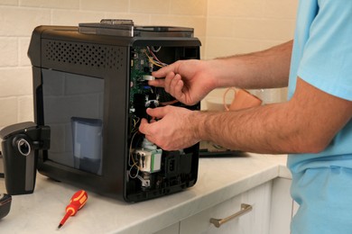 Photo of Man fixing coffee machine at table indoors, closeup