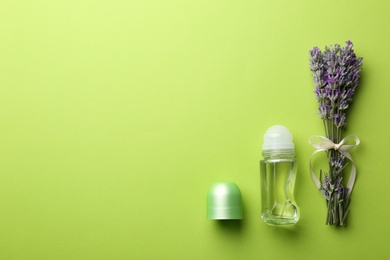 Female deodorant and lavender flowers on green background, flat lay. Space for text