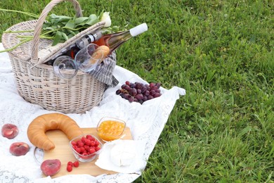 Picnic basket with tasty food, flowers and cider on blanket outdoors