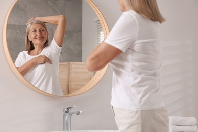 Photo of Beautiful senior woman doing breast self-examination near mirror in bathroom