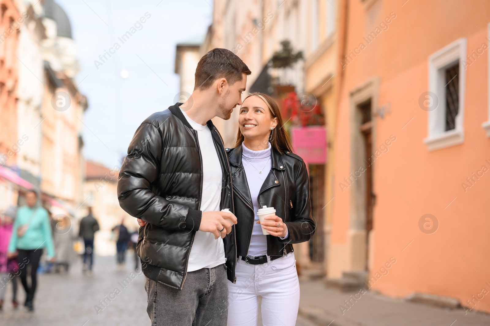 Photo of Lovely young couple with cups of coffee walking together on city street. Romantic date