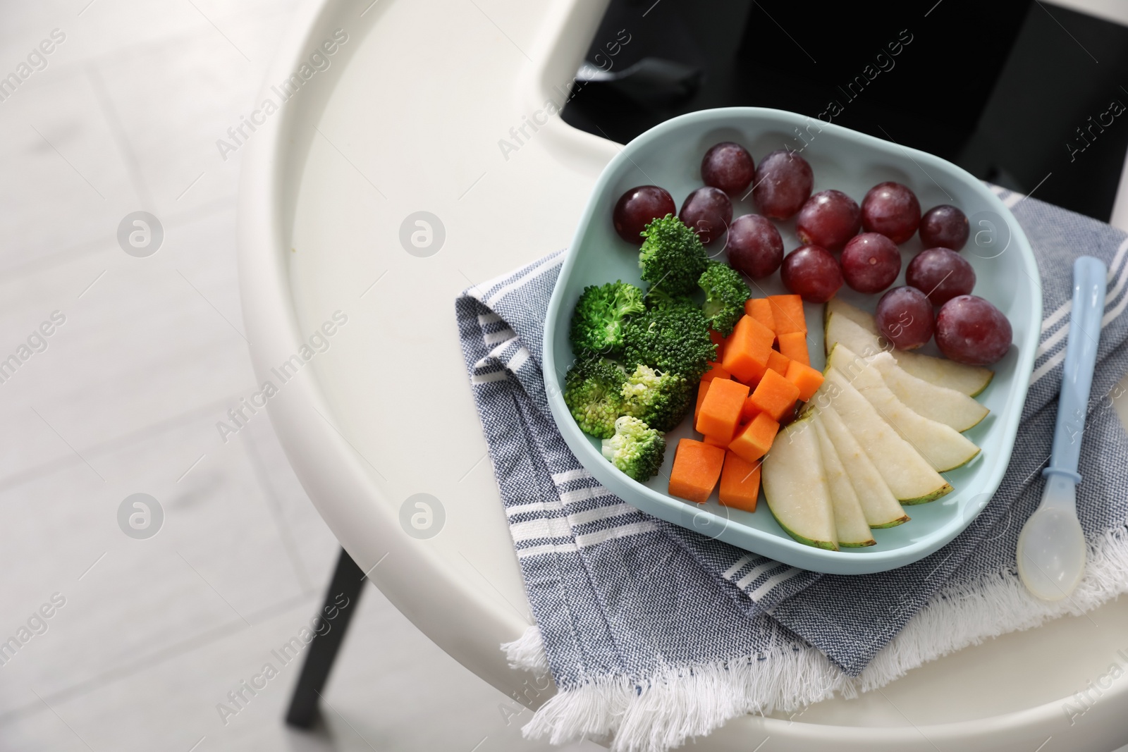 Photo of High chair with food in baby tableware on tray indoors, closeup. Above view