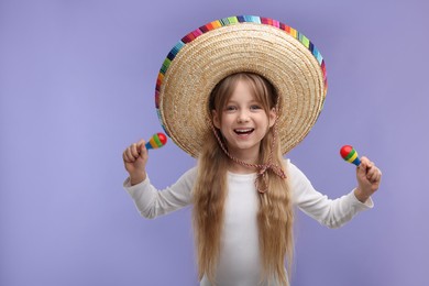 Photo of Cute girl in Mexican sombrero hat with maracas on purple background