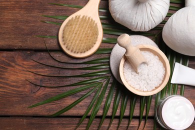 Flat lay composition with sea salt, spa products and green leaves on wooden table