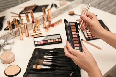 Photo of Professional makeup artist with eyeshadow palette 
and brush at dressing table, closeup