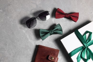 Photo of Stylish color bow ties, box, wallet and sunglasses on gray marble background, flat lay