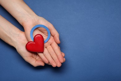 Photo of Woman showing blue paper circle as World Diabetes Day symbol and red heart on color background, top view with space for text