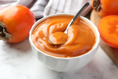 Delicious persimmon jam and fresh fruits on white marble table, closeup