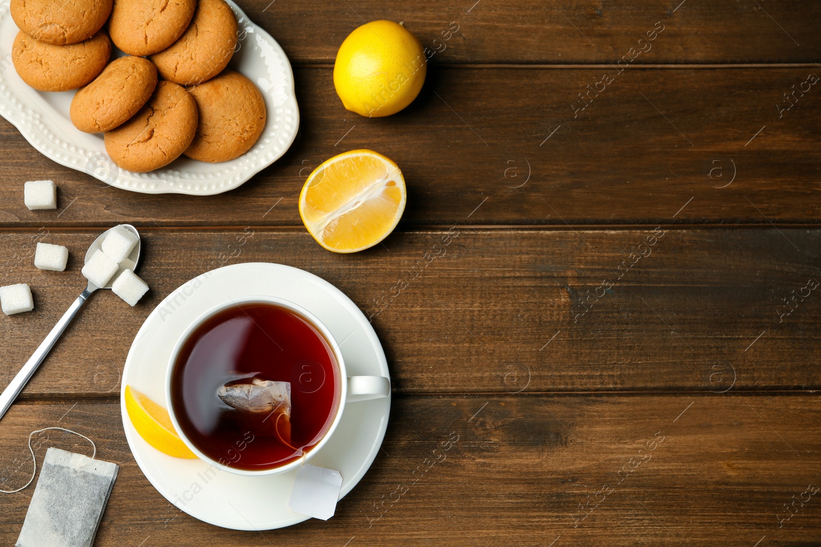 Photo of Flat lay composition with tea bag in ceramic cup of hot water, cookies and lemon on wooden table. Space for text