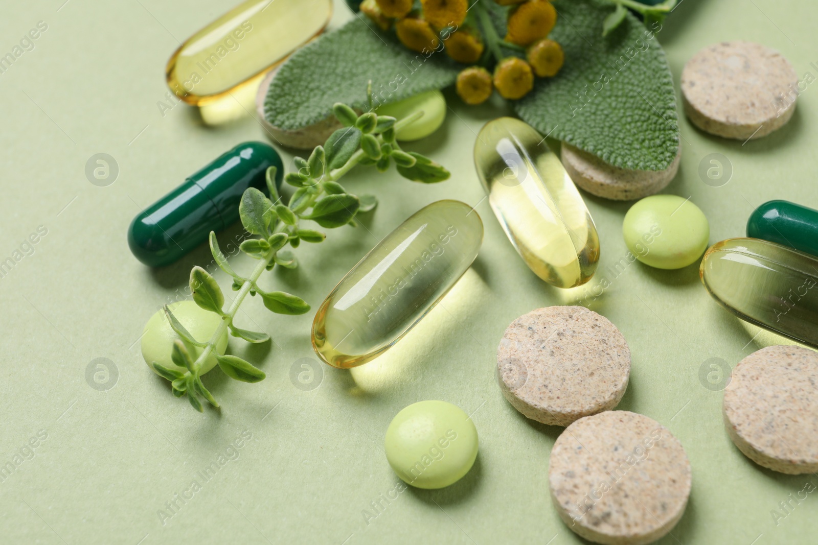 Photo of Different pills and herbs on light green background, closeup. Dietary supplements
